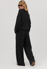 Czarny, oversize sweatshirt i szerokie spodnie wykonane z miękkiego materiału. Projekt cechuje minimalistyczny styl i luźny krój z kieszeniami.