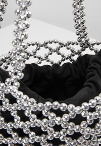 Pochette en tissu noir à l'intérieur d'un petit sac à main avec un motif en treillis fait de perles argentées brillantes.