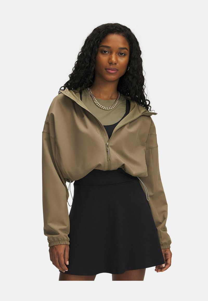 Khaki zip-up jakke med hætte, der har en løs pasform, elastiske manchetter og en glat tekstur, parret med en sort nederdel.