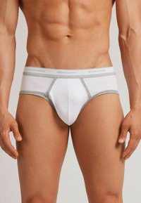 Weiße Herrenunterwäsche mit grauen Akzenten, die eine enge Passform, einen elastischen Bund mit "intimissimi"-Logo und eine glatte Baumwollstruktur aufweist.