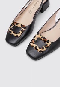 Zapatos de tacón de cuero negro con punta cuadrada y acento de piel de leopardo en la parte delantera. Presentan un tacón robusto y un diseño de lado abierto.
