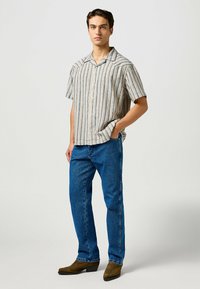Korte mouwen, geknoopte blouse met horizontale strepen in beige en marineblauw, gecombineerd met blauwe jeans en bruine laarzen met hak.