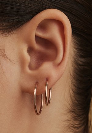 Boucles d'oreilles créoles en or rose avec une finition lisse et polie, présentées aux côtés d'un gros plan de l'oreille pour donner une référence de taille.