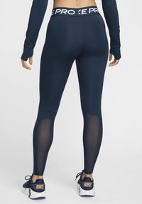 Marinblå leggings med bred midjeband som har "PRO"-logotyp, meshpaneler längs sidorna, kombinerat med svarta Nike träningsskor.