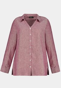 Camicia in lino botton-up in una sfumatura di rosa chiaro, con scollo a V, maniche lunghe e spacchi laterali. Presenti bottoni trasparenti lungo il davanti.