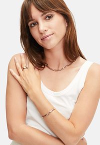 Roze gouden ketting en armband met onderling verbonden schakels. Model draagt een witte tanktop, waarop de sieraden prominent zichtbaar zijn.