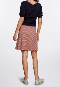 Granatowy sweter z krótkimi rękawami w połączeniu z czerwoną i białą wąską spódnicą w kształcie dzwonu oraz miętowymi trampkami, widoczne z tyłu.