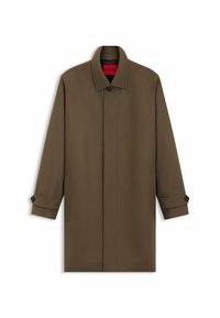 Brun yderjakke med lige snit, med knaplukning, to sidelommer og et rødt indvendigt etikette. Glat stof, struktureret krave.