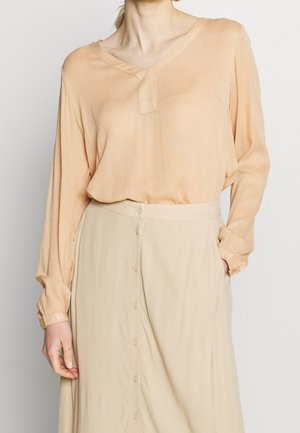 Blouse pêche avec un col en V et des manches longues, fabriquée à partir d'un tissu léger. Assortie d'une jupe beige avec des boutons sur le devant et une texture douce.