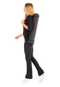 Black yoga mat rolled on shoulder, textured surface, carried by a person in black top and leggings, wearing white shoes, walking.