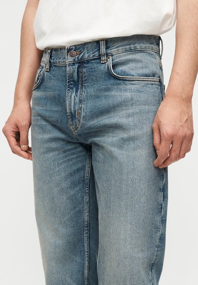 Τα ανοιχτό μπλε τζιν έχουν άνετη εφαρμογή, σχεδιασμό με πέντε τσέπες, διακριτικές ρυτίδες και ραφές με αντίθετο χρώμα κατά μήκος των ραφών.