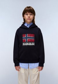 Sudadera negra de algodón, con una bandera noruega bordada y el texto "Napapijri geographic." Llevada sobre una camisa de color azul claro.