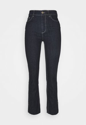 Tumma farkut korkealla vyötäröllä, kapea malli ja kevyt levennys helmassa. Ominaisuuksiin kuuluu kontrastiväriset saumat ja etupainikekiinnitys.