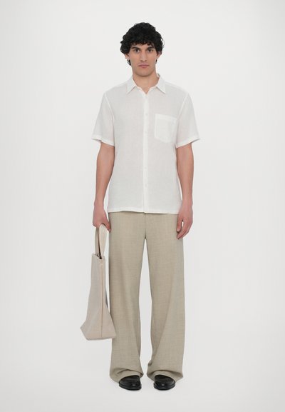 Camisa leve de linho branca de manga curta com fecho de botão e bolso no peito, combinada com calças largas bege e sapatos pretos.