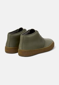 Stivaletti alla caviglia in pelle verde oliva con suola in gomma marrone texturizzata. Presentano cuciture minime e un logo impresso sul tallone.