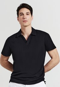 Polo nero con superficie texturizzata, maniche corte e colletto profondo e aperto. Vestibilità aderente al corpo, che evidenzia un design elegante.
