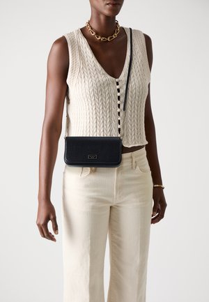 Black leather crossbody bag with a smooth texture, rectangular shape, and gold hardware detail, worn with a cream knit top and light pants.