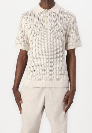 Camisa polo de punto beige con cuello acanalado, mangas cortas y un patrón texturizado con cierre de tres botones.