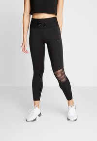 Leggings sportivi neri con vita alta, caratterizzati da un pannello in rete con dettagli logo. Il materiale è morbido, con un design semi-attillato.