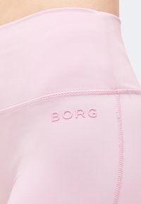 Κοντινή λήψη ανοιχτόροζ κολαν με ψηλή μέση και ανάγλυφο λογότυπο "BORG" κοντά στη ραμμένη πλευρική ραφή.