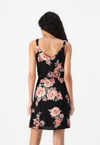 Robe florale noire avec un dos en V, ornée de grandes roses roses et crème, avec des fines bretelles et une taille élastique, fabriquée en tissu léger.
