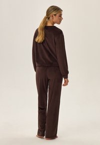 Brązowy dres z weluru, składający się z długiego rękawa bluzki oraz luźnych spodni, o miękkiej fakturze i minimalistycznych elementach designu.