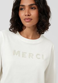 Ecruowa bluza z napisem "MERCI" wykonanym z perłopodobnych koralików, z okrągłym dekoltem i miękką fakturą tkaniny.