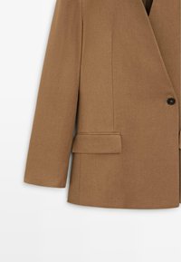 Bruine op maat gemaakte blazer met lange mouwen, sluiting met één knoop en een klepzak aan de linkerkant.