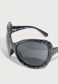 Μαύρα γυαλιά ηλίου με στρογγυλεμένους φακούς. Διακοσμημένα με λαμπερά κρύσταλλα Swarovski γύρω από το πλαίσιο. Λεία υφή πλαστικού, κομψός σχεδιασμός.