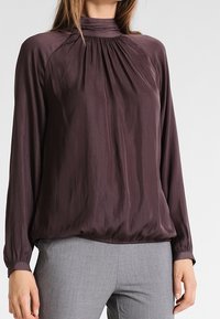 Lilla langærmet bluse med samlet halsudskæring, let løs pasform og elastisk talje; glat tekstur, ingen synlige mønstre eller detaljer.