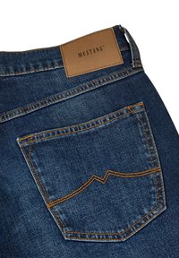 Jeans de mezclilla azul oscuro con un bolsillo trasero prominente con costuras en zigzag y una etiqueta de cuero marrón claro con el grabado "MUSTANG".
