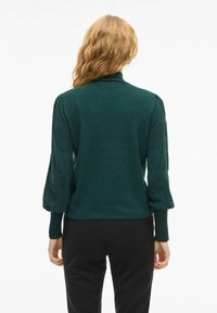 Maglione verde con colletto alto, corpo aderente e maniche a palloncino. Realizzato in tessuto morbido, presenta una texture liscia e un colore uniforme.