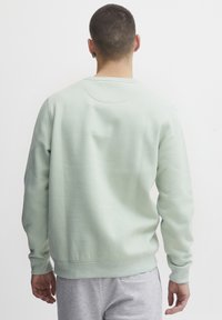 Felpa di un verde menta chiaro con colletto rotondo, polsini e orlo a coste, realizzata in un morbido misto cotone, con una texture semplice.