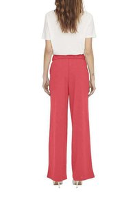 Pantalons larges en tissu corail vif avec une texture lisse, dotés d'une taille plate et de poches latérales, associés à un haut blanc.