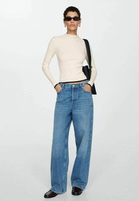 Tætsiddende cremefarvet ribbet langærmet top, brede blå denimjeans, sorte solbriller, sort håndtaske og blanke sorte sko.