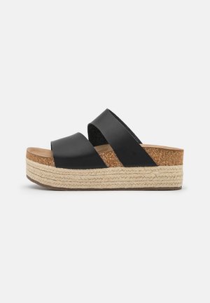 Sandalia de plataforma negra con dos anchas correas de cuero y una suela tejida con textura y plantilla de corcho, vista lateral.