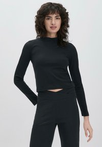 Schwarzes langärmliges Crop-Top mit einem Stehkragen und einem Cut-Out-Detail vorne. Der Stoff sieht glatt und dehnbar aus und eignet sich gut für aktive Kleidung.