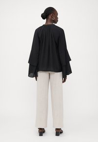 Black long-sleeve blouse with ruffled cuffs, gathered back detail, paired with beige linen wide-leg pants and black heeled sandals.