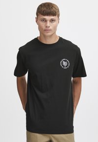 Sort bomulds T-shirt med korte ærmer, der har en hvid cirkulær grafik med tekst på venstre brystområde.