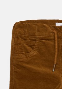 Bruna kordflortbyxor med mjuk textur, elastisk midja, dragsko-stängning och framfick detaljer.