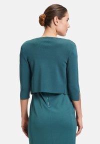 Turkusowy krótki top z rękawami o długości trzech kwart, teksturowana tkanina i warstwowy krój. Tył prezentuje ukryty zamek błyskawiczny w talii.