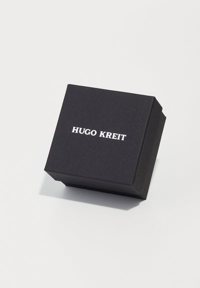 Crni pravokutni kutija od teksturiranog papira, s imenom "HUGO KREIT" napisanim bijelim, podebljanim fontom na vrhu.