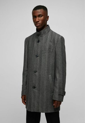 Grau meliertes Herringbone-Mantel mit hohem Kragen, sechs schwarzen Knöpfen, zwei seitlichen Taschen und einer kleinen Brusttasche, aus strukturiertem Stoff.