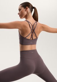 Lagani ljubičasti sportski grudnjak s krošem trakama, uparen s visokim ljubičastim tajicama, koje imaju glatku teksturu i suptilni brend.