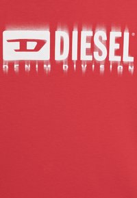 Rød t-skjorte laget av bomull med en jevn tekstur, med en stor hvit "DIESEL" logo og "DENIM DIVISION" trykt under i en falmet design.