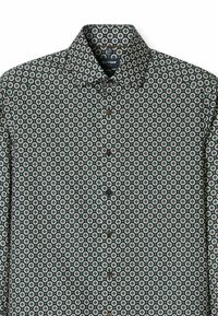 Grün gemustertes Hemd mit Button-Down-Kragen, das ein geometrisches Design in Weiß und Hellblau aufweist, sowie braune Knöpfe entlang der Knopfleiste.