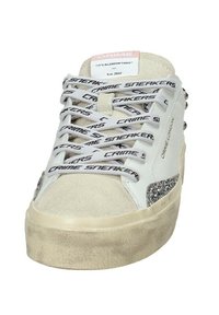 Sneaker bianca realizzata in materiali scamosciati e gomma, con lacci stampati neri, dettagli argentati sul lato e una suola piatta texturizzata.