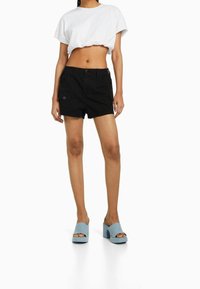 Černé cargo šortky s předními kapsami, zkombinované s krátkým bílým tričkem a světle modrými platformovými botami. Hladká textura tkaniny.
