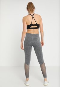Czarny stanik sportowy z krzyżującymi się ramiączkami, połączony z szarymi legginsami o wysokim stanie z siateczkowymi panelami na dolnej części nóg.