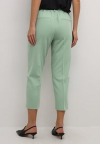 Pantaloni cropped verde menta con vita elastica e due tasche posteriori, abbinati a scarpe nere con tacco e una maglietta scura.